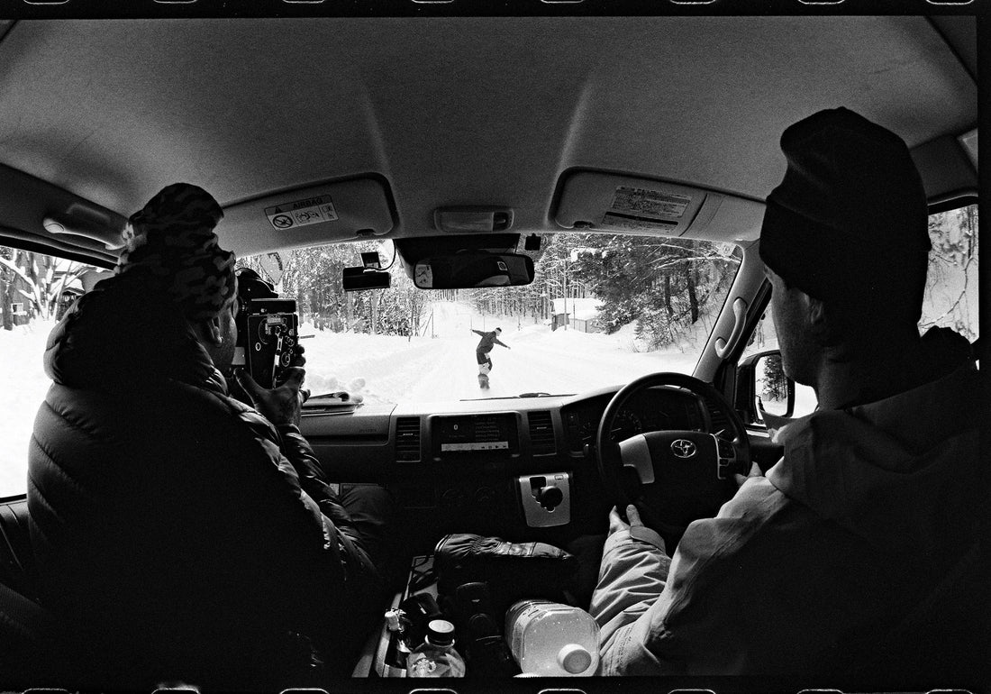 Jonah Schacter burns film while Avery Cloninger keeps a safe distance from Logan Boyd, riding down a snow-covered road, Kamifurano, Japan
