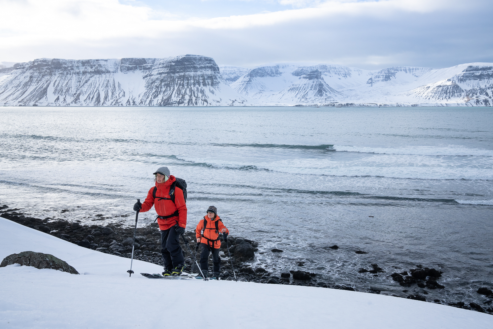 Elena Hight and Robin Van Gyn splitboarding above a breaking wave. Westfjords, Iceland.